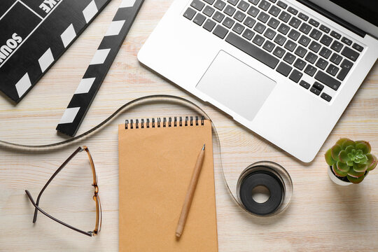 Notebook with film, movie clapper and laptop on light wooden background