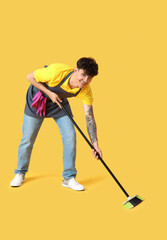 Male janitor with broom on yellow background