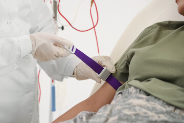 Doctor preparing female soldier for blood transfusion in clinic, closeup