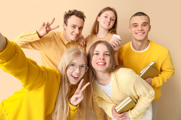 Group of students with books and cup of coffee taking selfie on pale yellow background