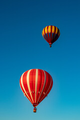Two red and yellow Hot Air Balloons soaring against a bright blue sky