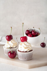 Board with tasty cherry cupcakes on light background