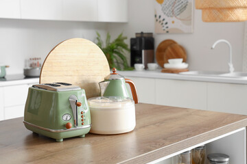 Toaster, electric kettle, juicer and cutting board on wooden table in modern kitchen