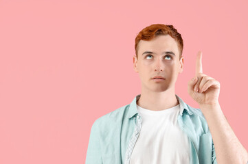 Naklejka premium Thoughtful young redhead man pointing at something on pink background