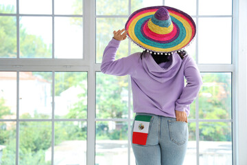 Young woman in sombrero hat with Mexican flag at home, back view