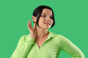 Young woman with hearing aid on green background, closeup