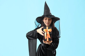 Young Asian woman dressed as witch with Halloween gift on blue background