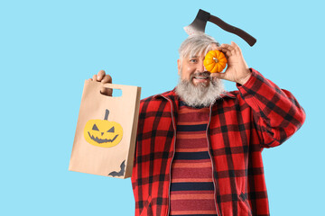 Mature man dressed for Halloween with pumpkin and gift bag on blue background