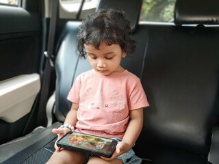 An Asian little girl sitting backseat in the car and using a smart phone
