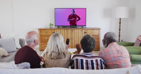 Senior diverse friends watching tv with african american male rugby player catching ball on screen - Powered by Adobe