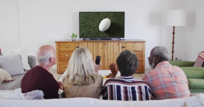 Senior diverse friends watching tv with rugby ball at stadium on screen