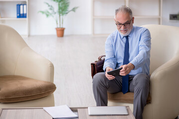 Old male employee playing smartphone games at workplace