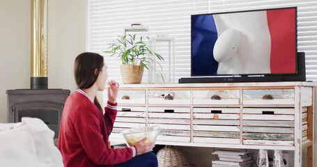 Caucasian woman watching tv with rugby ball on flag of france on screen - Powered by Adobe