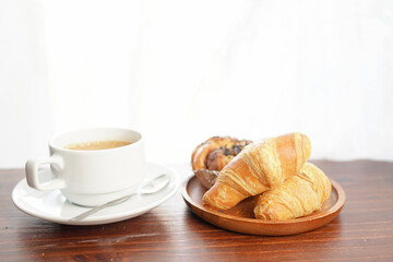 Croissants and coffee on the table by the curtained window.