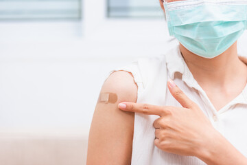 Asian young woman smile she is pointing to adhesive plaster on arm her vaccinated after getting immunity vaccine COVID-19 prevent