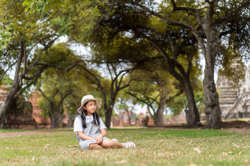 asian child or kid girl travel to sit squat on grass lawn in garden archaeological site and pagoda ruins in wat phra si sanphet temple at ayutthaya old ancient Thailand for people study retro historic