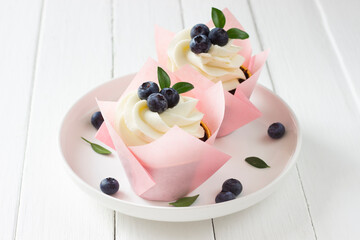 Cupcakes  with  blueberries decorated of pink wrapper, white plate, white wooden board