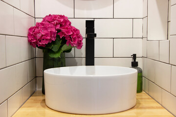 Interior of bathroom sink bowl on wooden table, flowers and bath accessories