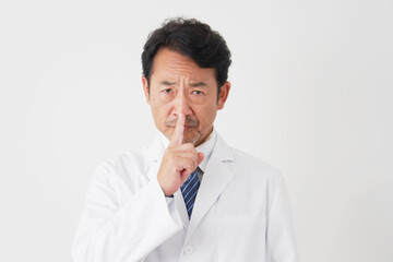 内緒のポーズをする中年の医師　白背景