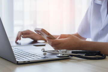 Doctor using mobile phone and digital tablet with laptop computer and stethoscope on office desk....