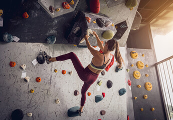 A strong female climber climbs an artificial wall with colorful grips and ropes.