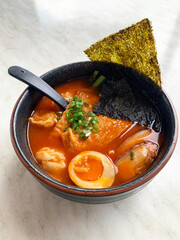 Japanese Korean ramen noodle in red tomato spicy chilli hot soup with onsen egg, seaweed, pork belly, bean curd, dumpling in bowl on white table asian cuisine halal food restaurant banquet cafe menu