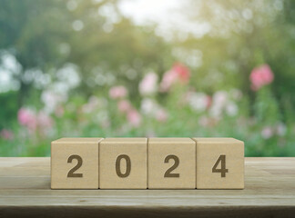 2024 letter on wood block cubes on wooden table over blur pink flower and tree in garden, Happy new...