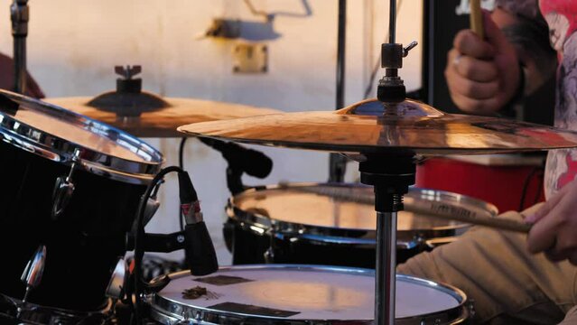 Hands of a drummer rapidly beating on drums with sticks in close-up. In the background a technician is correcting a cymbal. Live performance in the open air. Rock concert. Concept of creativity