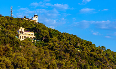 Wooded slope of mountain coast of Cap Ferrat cape and Saint-Jean-Cap-Ferrat resort town with Semaphore Tower at French Riviera of Mediterranean Sea near Nice in France