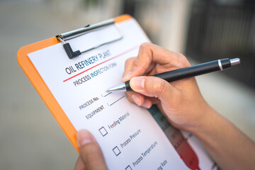 Action of a chemical engineer is using the pen to checking on oil refinery distillation process inspection form. Industrial working scene,close-up and selective focus.