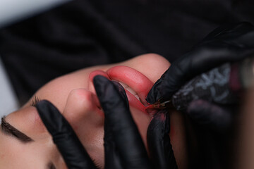 Macro photo of the process of applying permanent makeup to the skin of the lips. Delicate permanent lip makeup for blondes