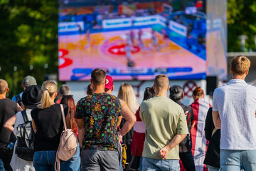 Crowd of people watching basketball game on big tv screen