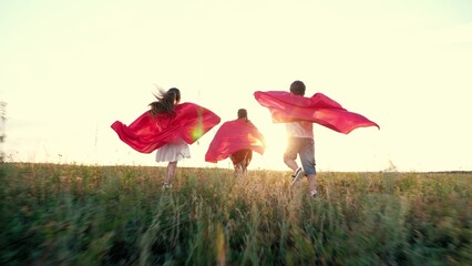 Little children wearing red capes play superheroes running across field