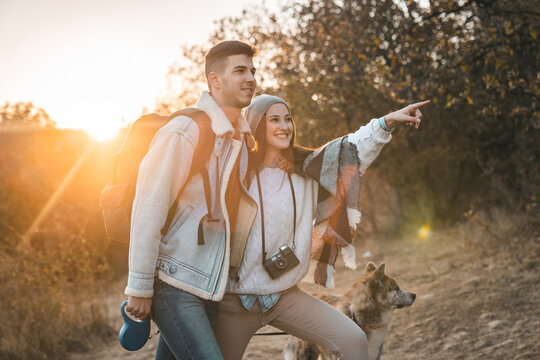 Young man and woman with dog taking a walk in woods. They are smiling while he is holding the leash. Hiking in nature with pet.