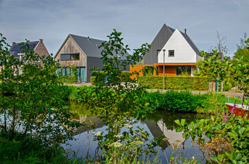 Rijswijk, The Netherlands, September 3, 2023: Modern houses reflecting in a canal in a green...