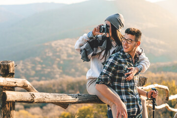 Happy couple sitting on a wooden fence and taking photos of nature during the hike. They are admiring their surroundings.