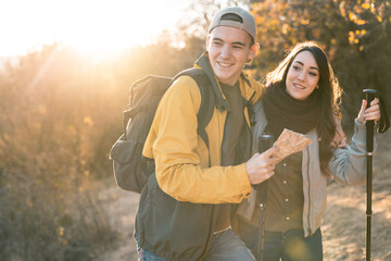 Two young people, a boy and a girl, holding hiking equipment and having a good time while walking...