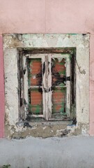 An old wooden window with old white paint is boarded up with bricks