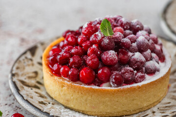 Close up of french dessert tart with fresh cowberry, cream and sugar powder on rustic background. Berry tartlet