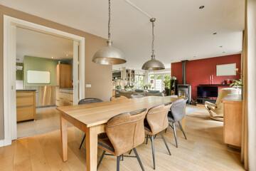 a dining room with wood flooring and red accent wall in the kitchen, living room is visible on the right side