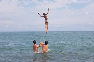 Happy child girl jumping in the sea. Kid having fun outdoors. Summer vacation and healthy lifestyle concept