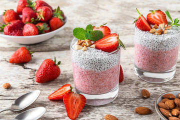 Vegan breakfast. Strawberry and vanilla chia pudding in glasses with fresh berries, nuts, mint and spoons on white rustic table