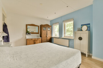 a bedroom with blue walls and white bedding in the corner, there is a large mirror on the wall