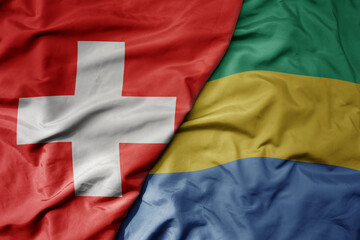 big waving national colorful flag of switzerland and national flag of gabon .