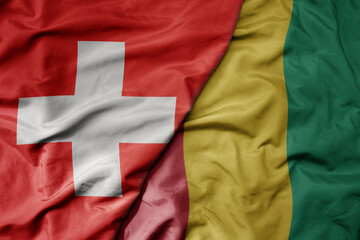 big waving national colorful flag of switzerland and national flag of guinea .
