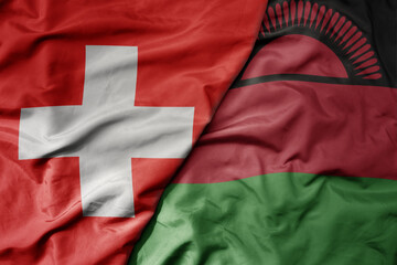 big waving national colorful flag of switzerland and national flag of malawi .