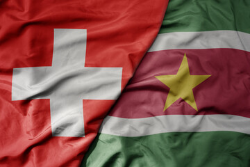 big waving national colorful flag of switzerland and national flag of suriname .