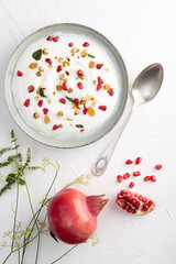 Yogurt with raisins, pistachios and pomegranate seeds in plate on green background. top view. Healthy breakfast, healthy eating concept