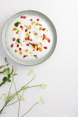 Yogurt with raisins, pistachios and pomegranate seeds in plate on green background. top view. Healthy breakfast, healthy eating concept