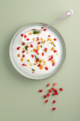 Yogurt with raisins, pistachios and pomegranate seeds in plate on green background. top view. Healthy breakfast, healthy eating concept